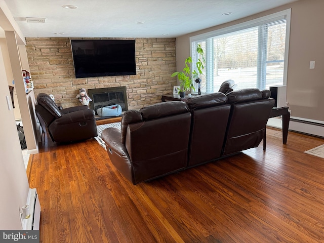 living room with a baseboard radiator, a stone fireplace, and dark wood-type flooring