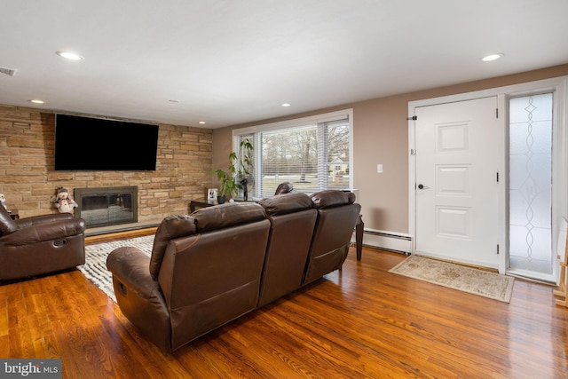 living room with wood-type flooring, a stone fireplace, and a baseboard heating unit