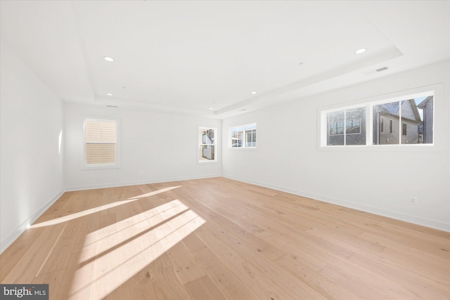 spare room with a tray ceiling and light hardwood / wood-style floors