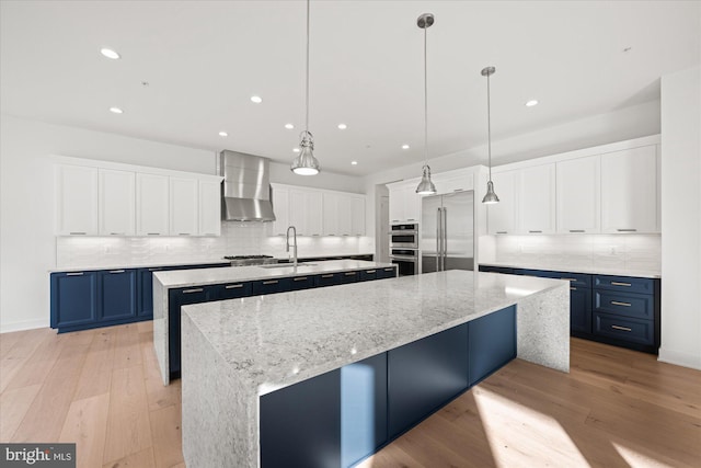 kitchen featuring blue cabinetry, a spacious island, stainless steel appliances, and wall chimney range hood