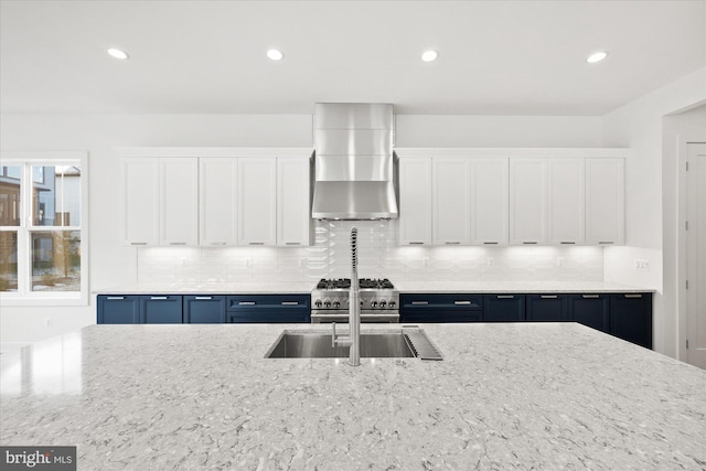 kitchen featuring high end range, wall chimney range hood, blue cabinetry, light stone counters, and white cabinetry