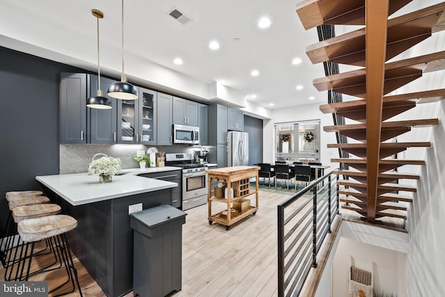 kitchen featuring kitchen peninsula, appliances with stainless steel finishes, backsplash, a kitchen breakfast bar, and hanging light fixtures