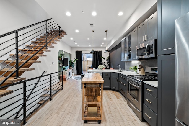 kitchen featuring sink, light hardwood / wood-style flooring, pendant lighting, gray cabinets, and appliances with stainless steel finishes