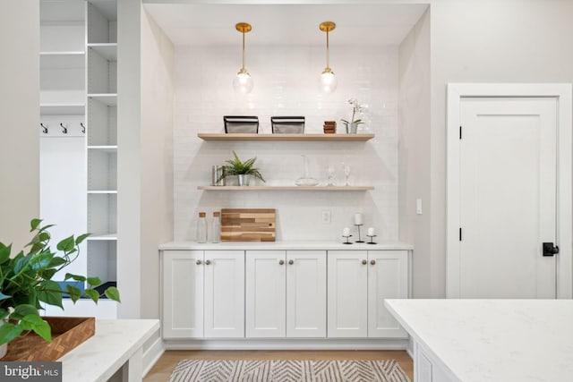 bar featuring pendant lighting, white cabinets, light hardwood / wood-style flooring, tasteful backsplash, and light stone counters