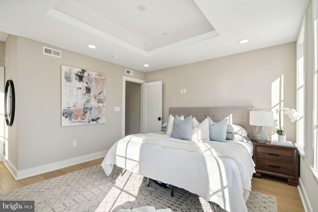 bedroom featuring a raised ceiling and light hardwood / wood-style flooring