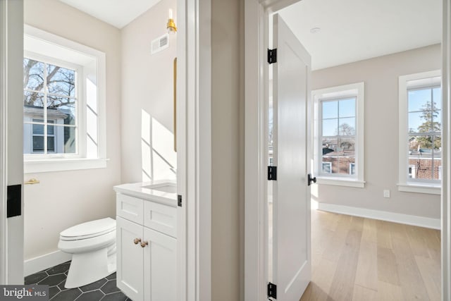 bathroom featuring wood-type flooring, vanity, a healthy amount of sunlight, and toilet