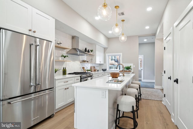 kitchen featuring white cabinetry, wall chimney range hood, a kitchen bar, a center island with sink, and high end appliances