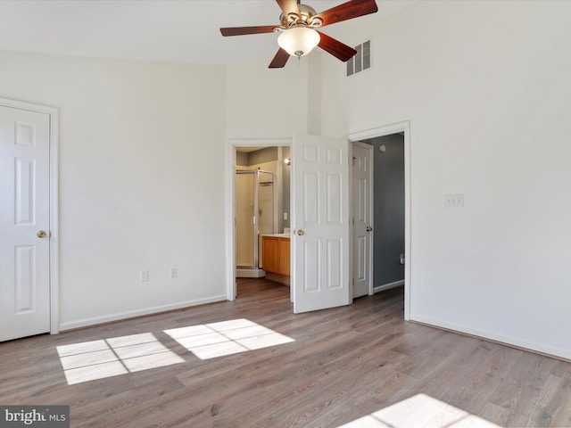 unfurnished bedroom featuring visible vents, baseboards, connected bathroom, a towering ceiling, and light wood-style flooring