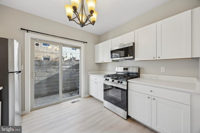 kitchen with stainless steel appliances, white cabinetry, light wood-type flooring, hanging light fixtures, and a notable chandelier