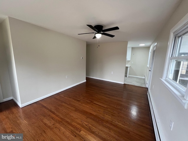 spare room with dark wood-type flooring, a healthy amount of sunlight, baseboard heating, and ceiling fan