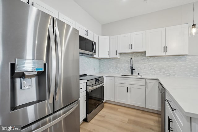 kitchen with pendant lighting, backsplash, white cabinets, sink, and appliances with stainless steel finishes