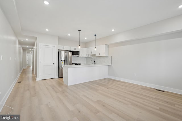 kitchen featuring stainless steel appliances, kitchen peninsula, pendant lighting, light hardwood / wood-style floors, and white cabinets