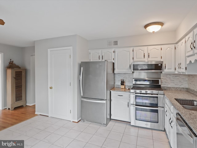 kitchen featuring decorative backsplash, light tile patterned floors, white cabinetry, and appliances with stainless steel finishes