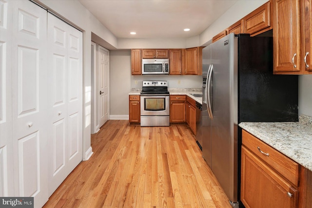 kitchen with light stone countertops, appliances with stainless steel finishes, and light hardwood / wood-style flooring