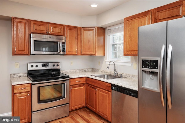 kitchen featuring sink, light stone counters, light hardwood / wood-style flooring, and appliances with stainless steel finishes