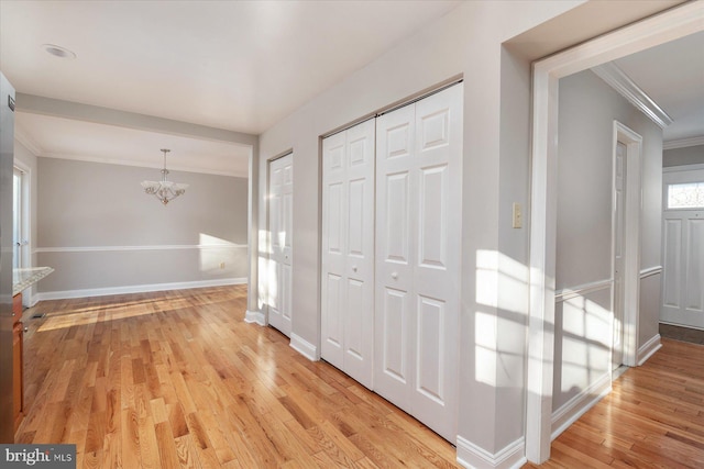 corridor with crown molding, an inviting chandelier, and light hardwood / wood-style flooring