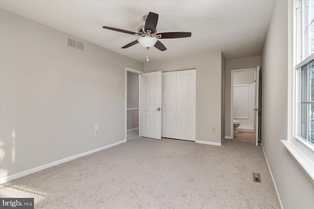 unfurnished bedroom featuring ensuite bath, light colored carpet, ceiling fan, and a closet