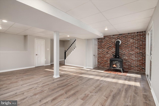 basement featuring hardwood / wood-style floors, a drop ceiling, and a wood stove