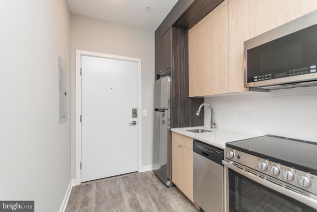 kitchen featuring electric panel, sink, light wood-type flooring, light brown cabinetry, and appliances with stainless steel finishes