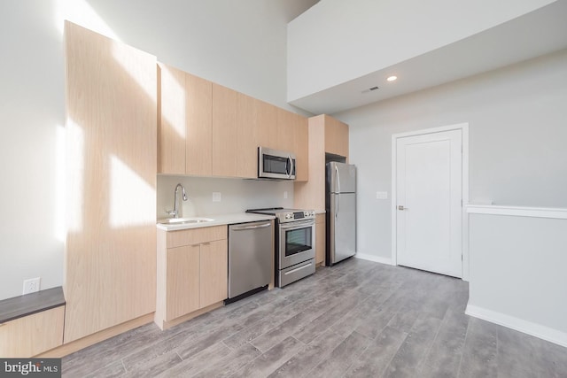 kitchen featuring light brown cabinets, sink, a towering ceiling, light hardwood / wood-style floors, and stainless steel appliances