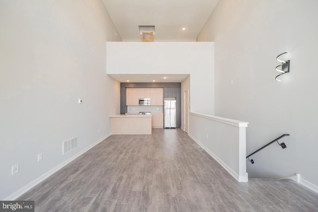 unfurnished living room with light wood-type flooring and a towering ceiling