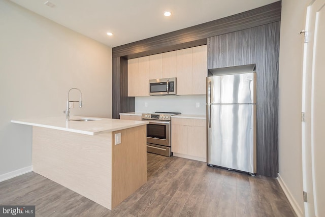 kitchen with a center island with sink, sink, dark hardwood / wood-style floors, light brown cabinetry, and appliances with stainless steel finishes