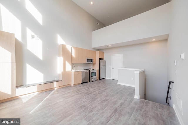 unfurnished living room featuring a towering ceiling, light hardwood / wood-style floors, and sink