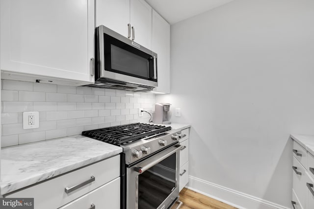 kitchen featuring white cabinets, decorative backsplash, light stone counters, and appliances with stainless steel finishes