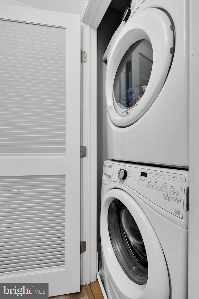 washroom with stacked washing maching and dryer and light hardwood / wood-style flooring