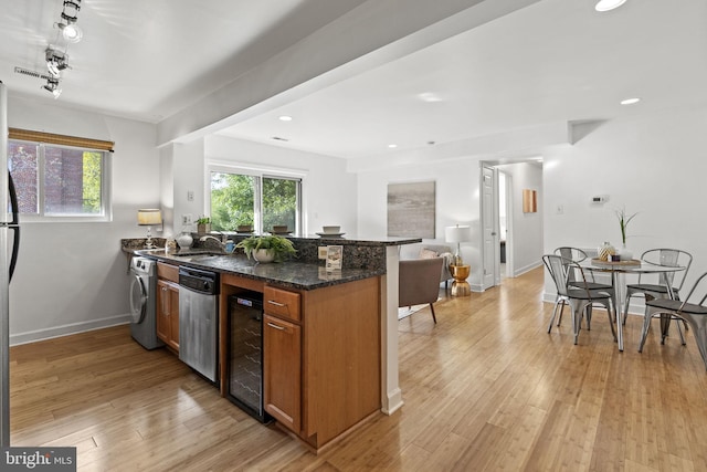 kitchen featuring washer / dryer, light hardwood / wood-style floors, beverage cooler, and dark stone countertops