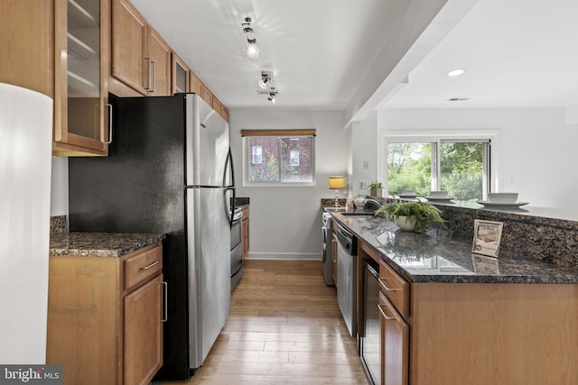 kitchen featuring dark stone countertops, rail lighting, light hardwood / wood-style floors, and appliances with stainless steel finishes