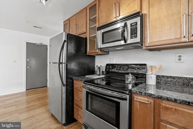 kitchen with stainless steel appliances, light hardwood / wood-style floors, and dark stone countertops