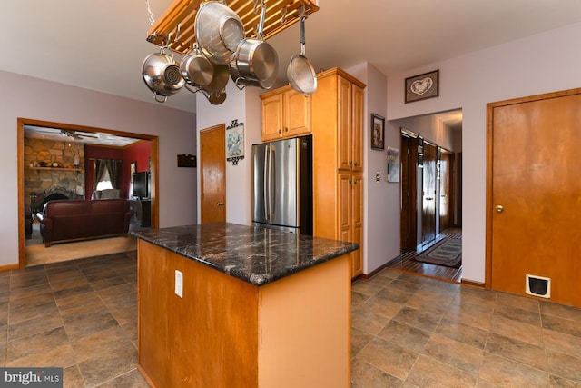 kitchen with a stone fireplace, stainless steel fridge, dark stone counters, and an inviting chandelier