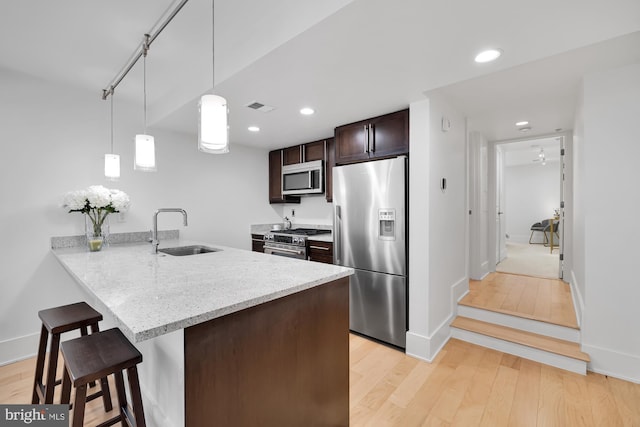 kitchen featuring light stone counters, stainless steel appliances, sink, pendant lighting, and light hardwood / wood-style flooring