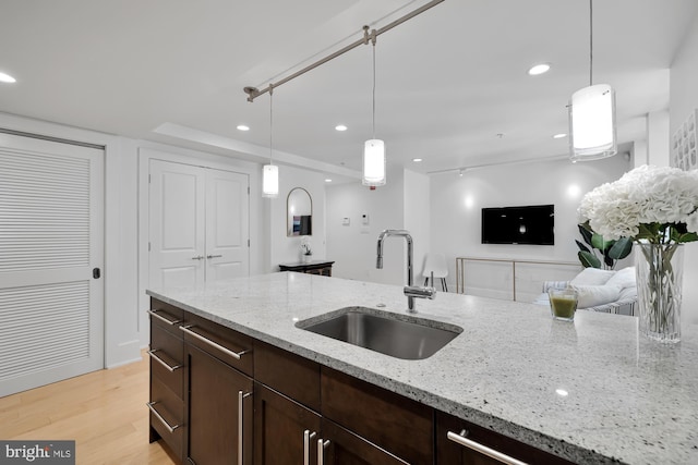 kitchen featuring pendant lighting, light hardwood / wood-style floors, light stone counters, and sink