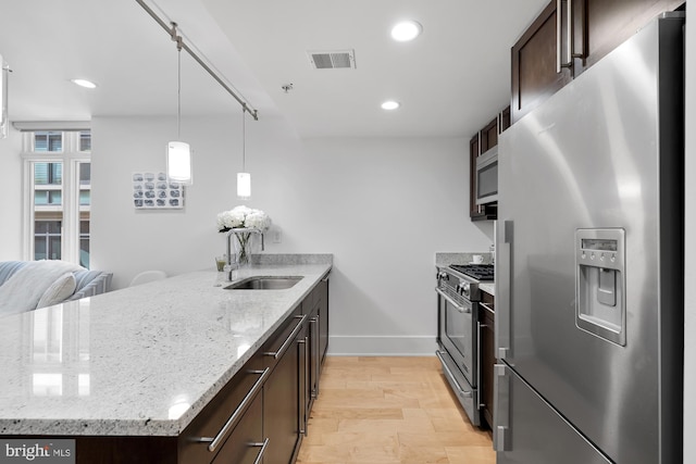 kitchen featuring light stone countertops, sink, stainless steel appliances, decorative light fixtures, and dark brown cabinets