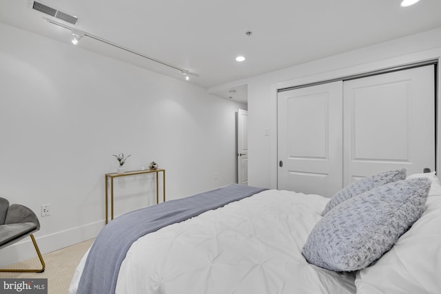 bedroom with track lighting, light carpet, and a closet