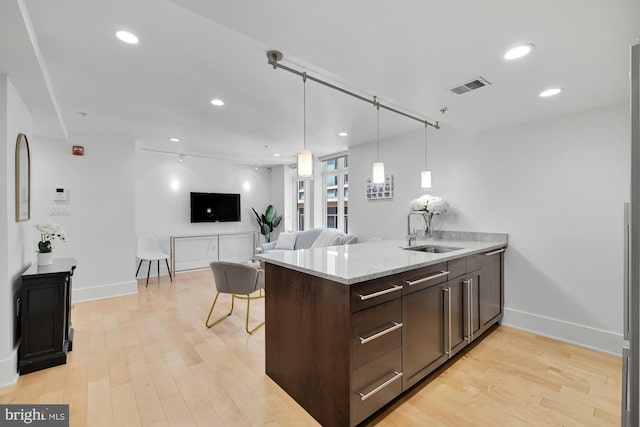 kitchen with sink, light stone counters, light hardwood / wood-style flooring, kitchen peninsula, and dark brown cabinets