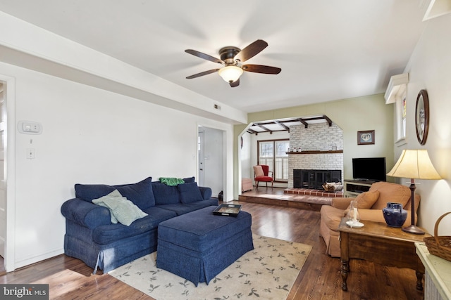 living room with ceiling fan, dark hardwood / wood-style flooring, and a brick fireplace