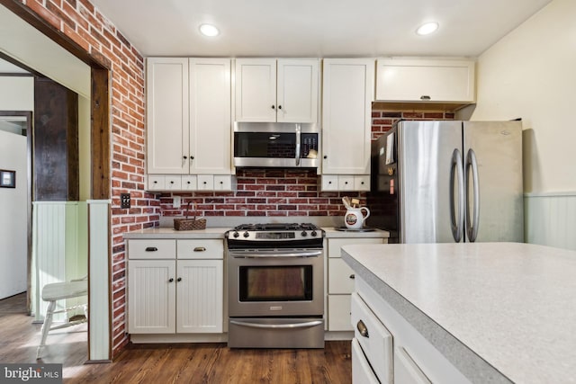 kitchen with white cabinetry, dark wood-type flooring, stainless steel appliances, brick wall, and backsplash