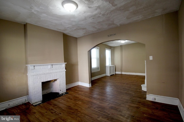 unfurnished living room with a fireplace, radiator heating unit, a textured ceiling, and dark hardwood / wood-style floors