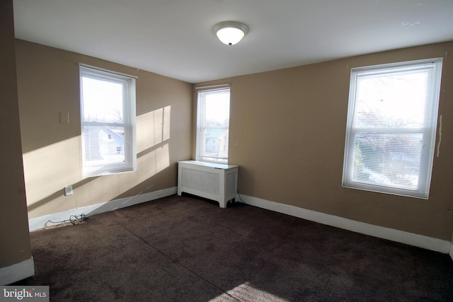 empty room featuring a wealth of natural light, radiator heating unit, and dark colored carpet