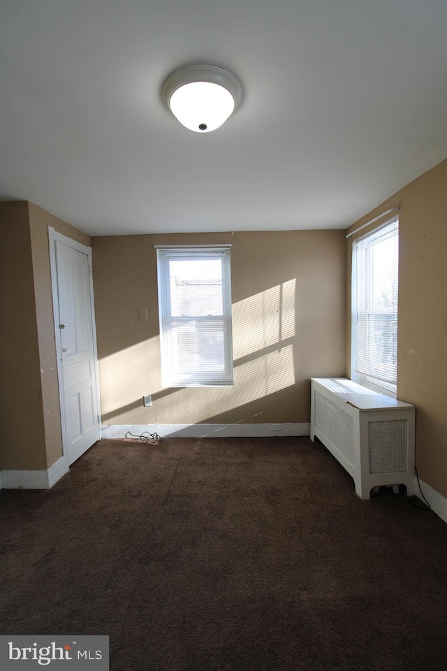 carpeted spare room featuring a healthy amount of sunlight and radiator heating unit