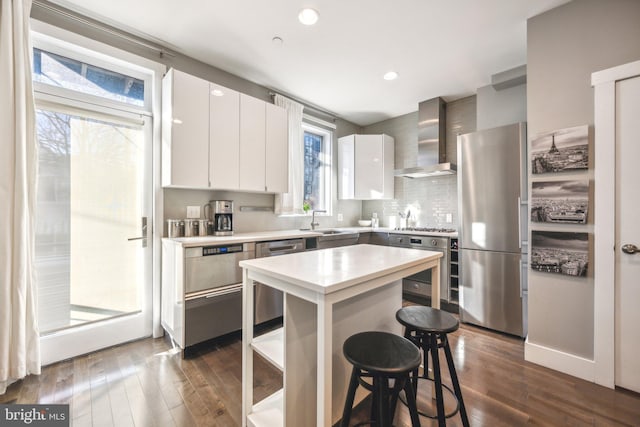 kitchen featuring wall chimney exhaust hood, a kitchen island, white cabinetry, and appliances with stainless steel finishes