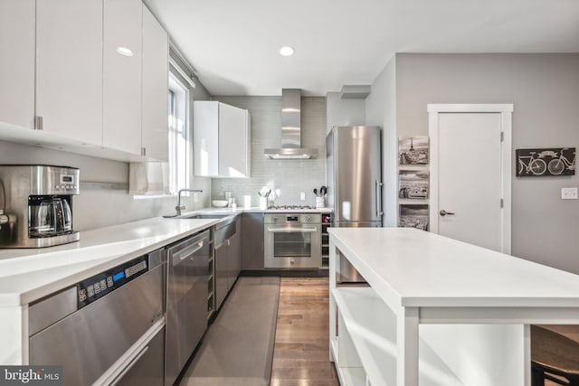 kitchen with wall chimney exhaust hood, appliances with stainless steel finishes, tasteful backsplash, white cabinetry, and wood-type flooring