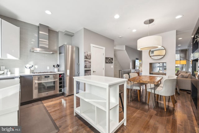 kitchen with pendant lighting, wall chimney exhaust hood, dark hardwood / wood-style floors, decorative backsplash, and appliances with stainless steel finishes