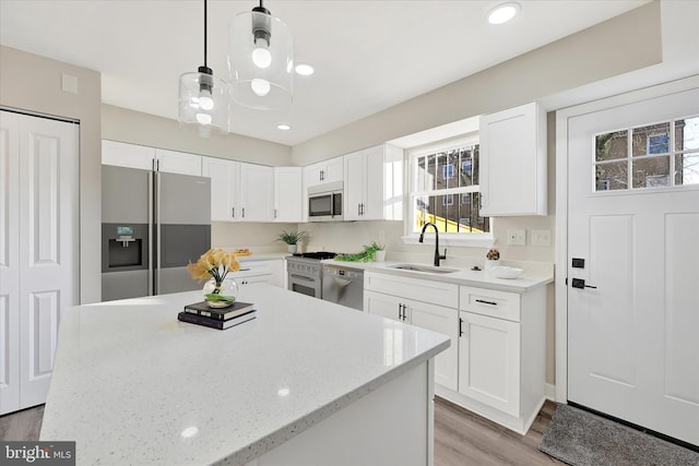 kitchen featuring pendant lighting, sink, white cabinetry, stainless steel appliances, and light stone counters