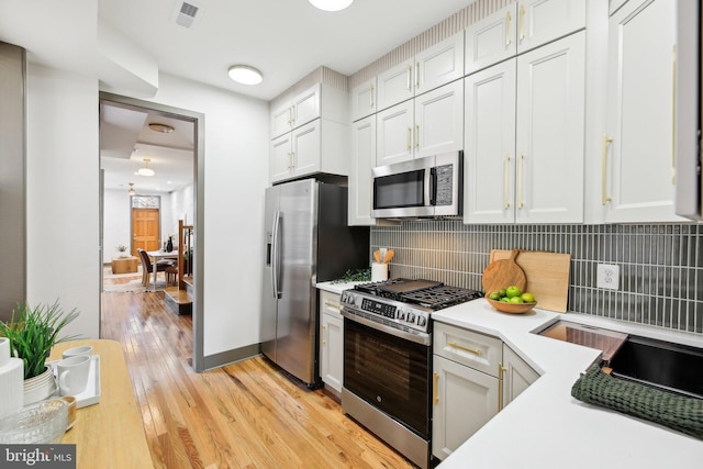 kitchen featuring white cabinetry, appliances with stainless steel finishes, light hardwood / wood-style floors, and tasteful backsplash