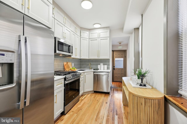 kitchen with sink, white cabinetry, stainless steel appliances, decorative backsplash, and light wood-type flooring