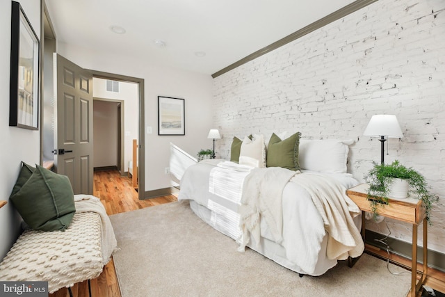 bedroom with light hardwood / wood-style floors and brick wall